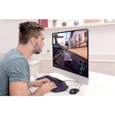 A man is playing a racing video game on a computer. The monitor displays a road on which he is driving a racing car.
