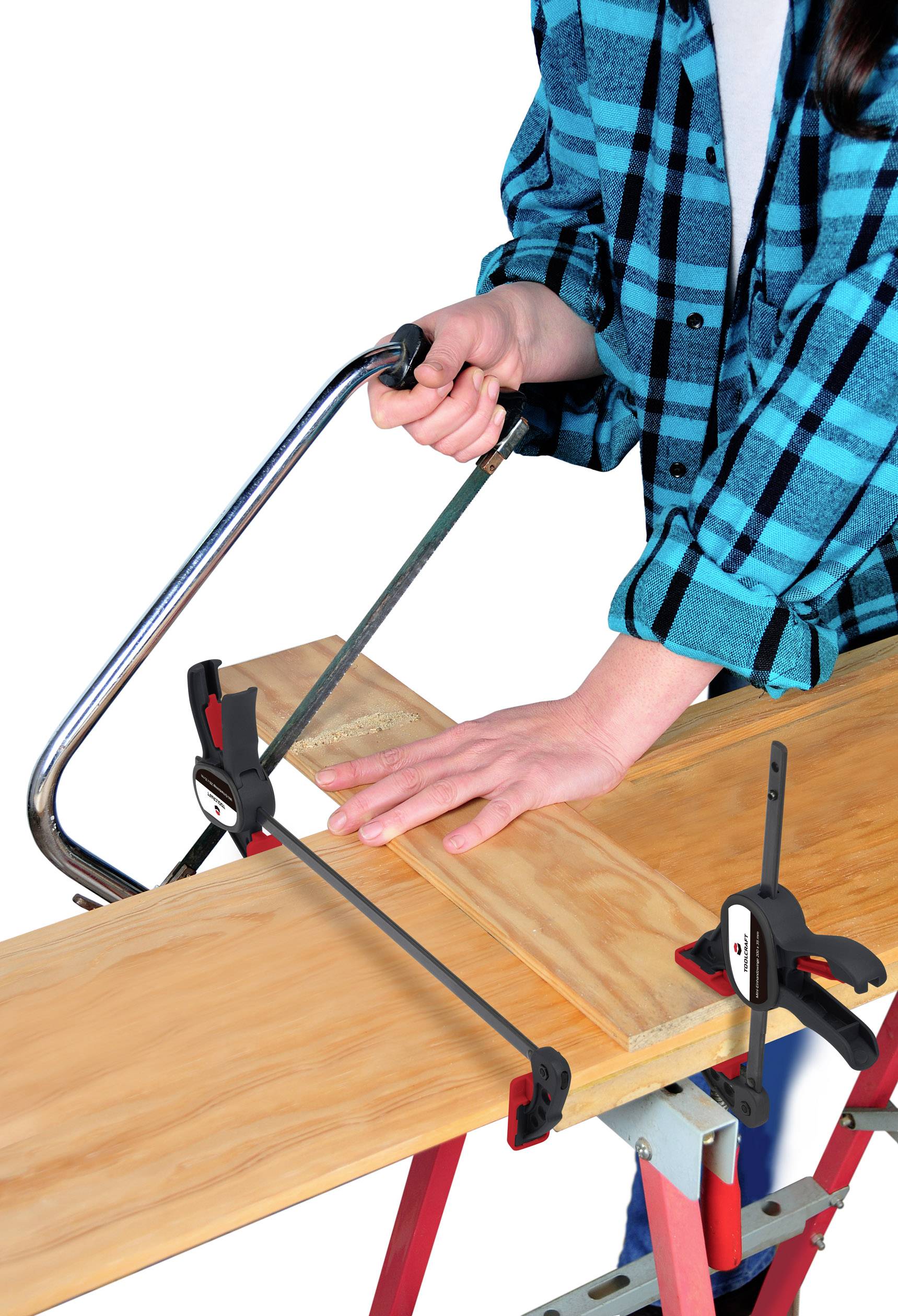 A person is sawing a wooden board with a handsaw, which is clamped in a workbench. They are wearing a checked shirt.