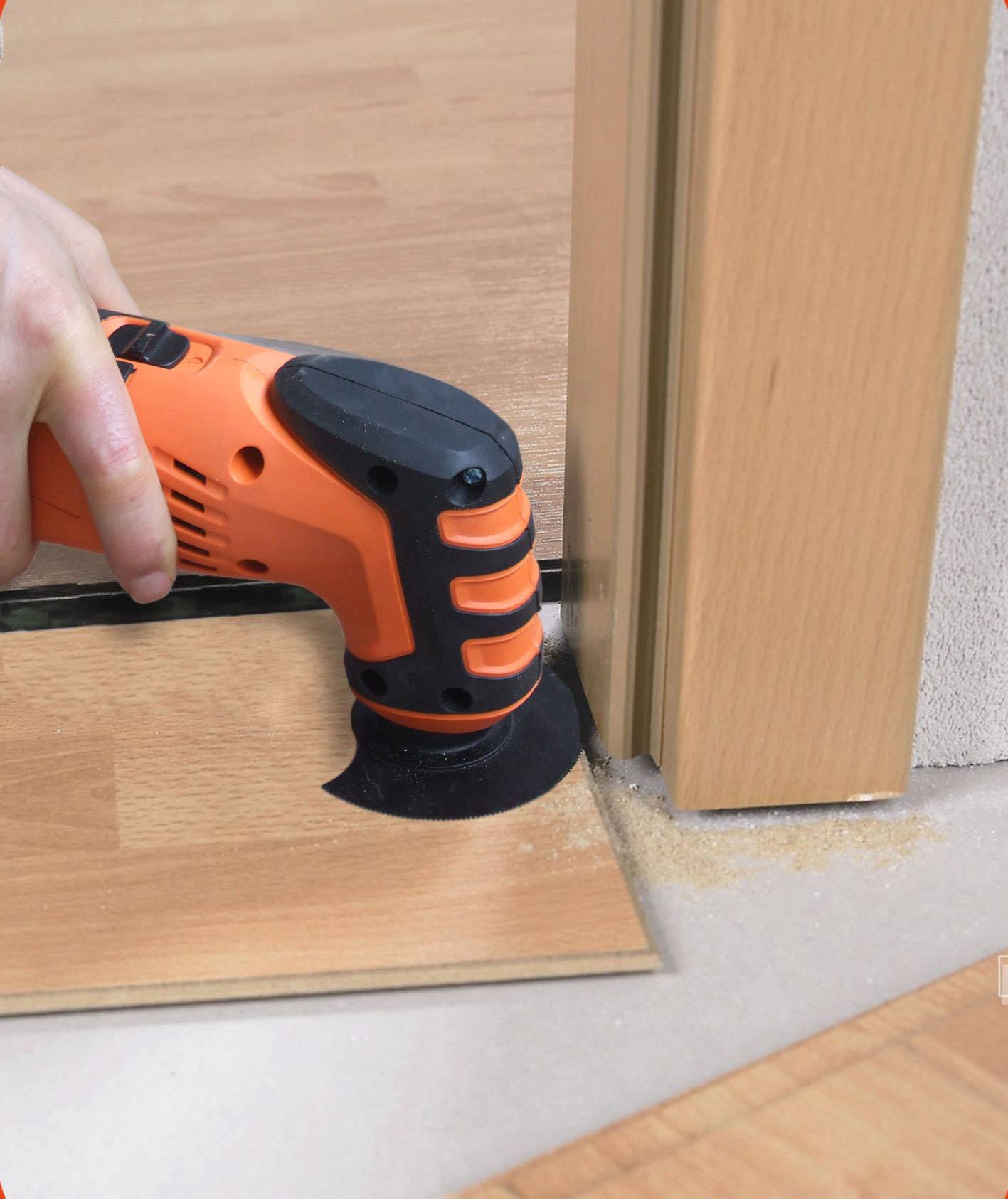 A person is cutting wood with an oscillating tool at the bottom edge of a door frame to adjust the flooring.