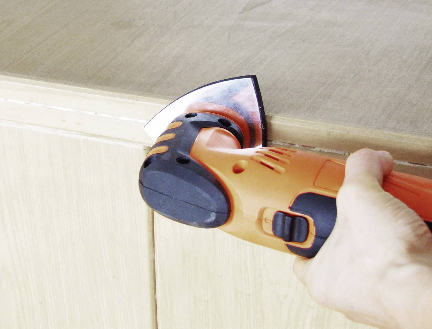 A hand holds an electric sanding tool, smoothing the edge of a wooden table.