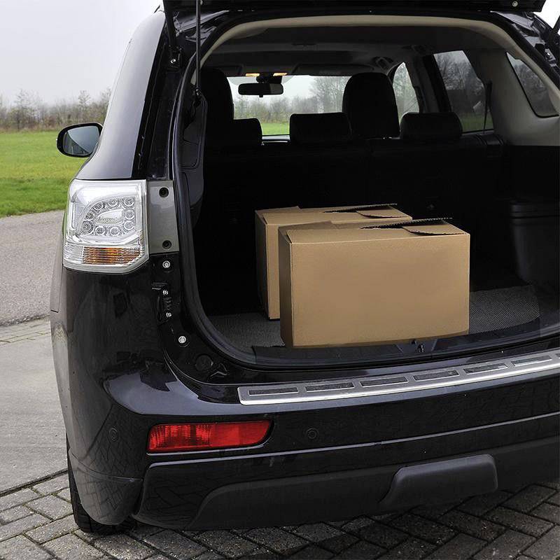 A car boot open and loaded with a large brown cardboard box is parked on a car park. A grassy area can be seen in the background.