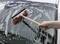 A hand is cleaning the windscreen of a car with a windscreen wiper and soapy water.