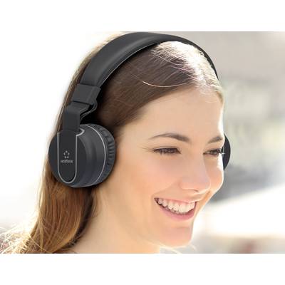 A woman is smiling and wearing large black headphones. The background is blurred.