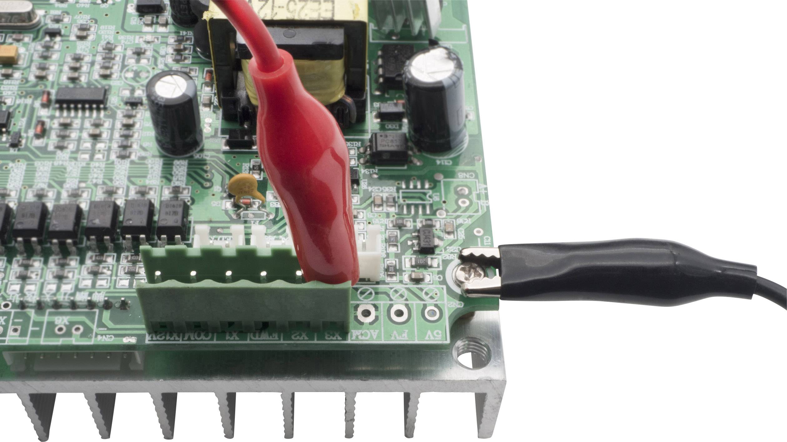 An electronic circuit board with components, to which two crocodile clips are connected, one red and one black.