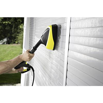 A person is cleaning a white venetian blind with a pressure washer. The background shows lawn and trees.