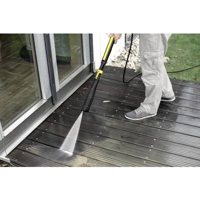 A person is cleaning a wooden terrace with a pressure washer next to a glass door.