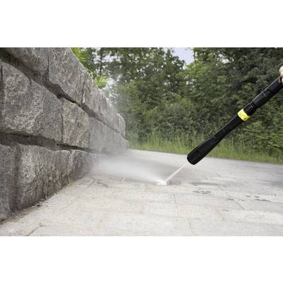 A person is cleaning the joints of a paved pathway next to a stone wall outdoors using a pressure washer.