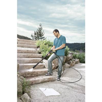 A man is cleaning an outdoor stone staircase with a pressure washer. It is sunny, and trees can be seen in the background.