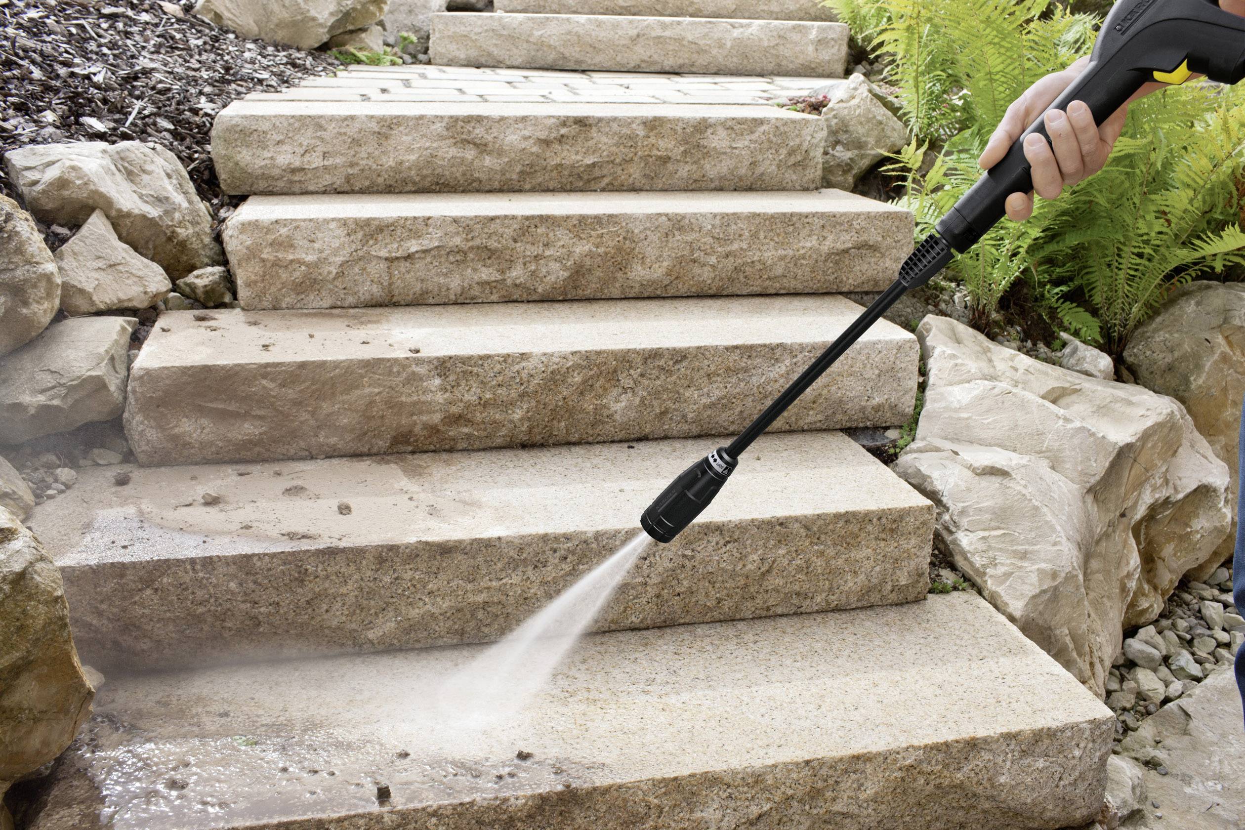 A person is cleaning stone steps with a pressure washer. Water droplets and dirt are visible on the steps.