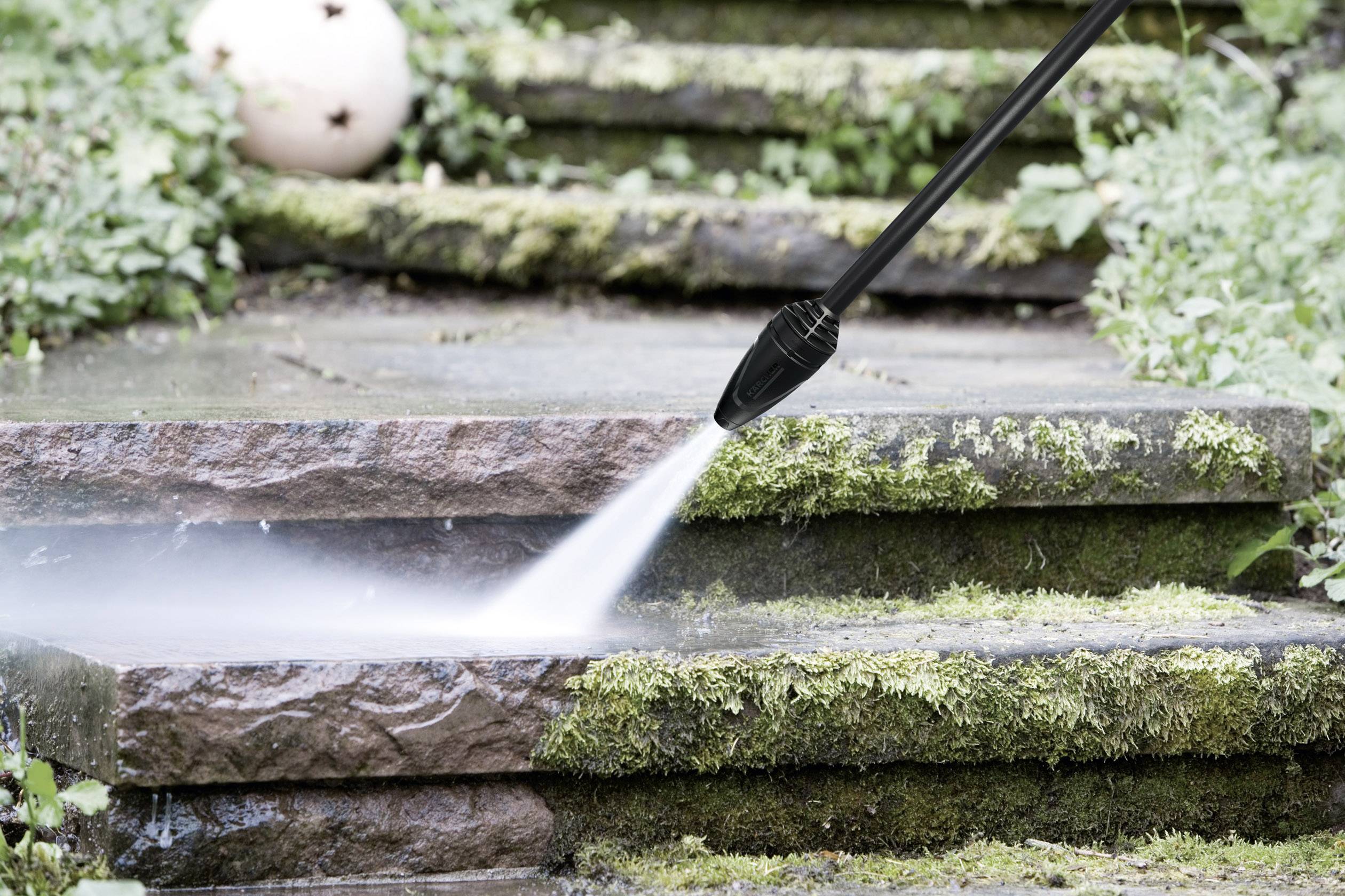A pressure washer sprays water onto moss-covered steps, cleaning algae and dirt. A garden ornamental sphere is visible in the background.