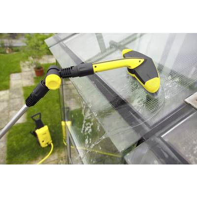 A window cleaner is cleaning a glass roof with an electric high-pressure washer. Water splashes are visible.