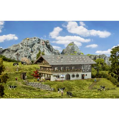 A miniature farmhouse in a mountainous landscape with cows, a hiker, and a blue sky in the background.