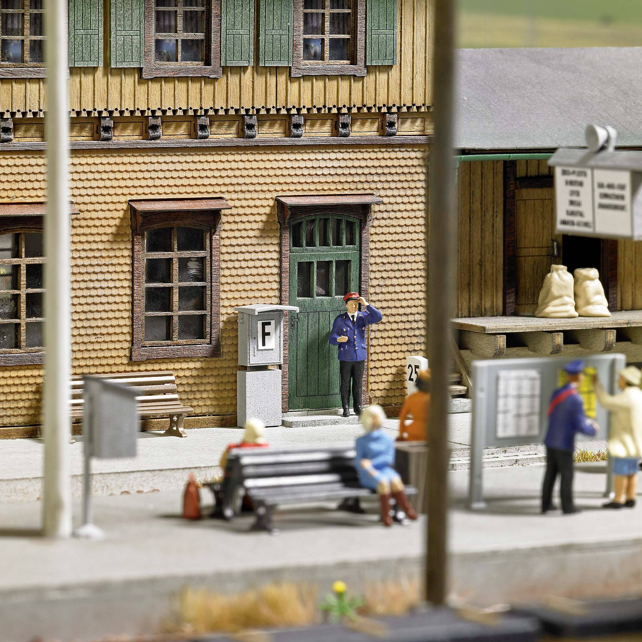 A miniature scene depicts people sitting on benches in front of a building. A man is standing and talking on the phone. There is a bus stop.