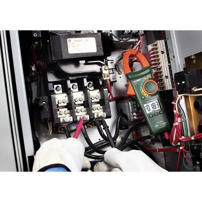 An electrician is measuring the electric current with a multimeter in a control panel. The display shows a value of 18.3.