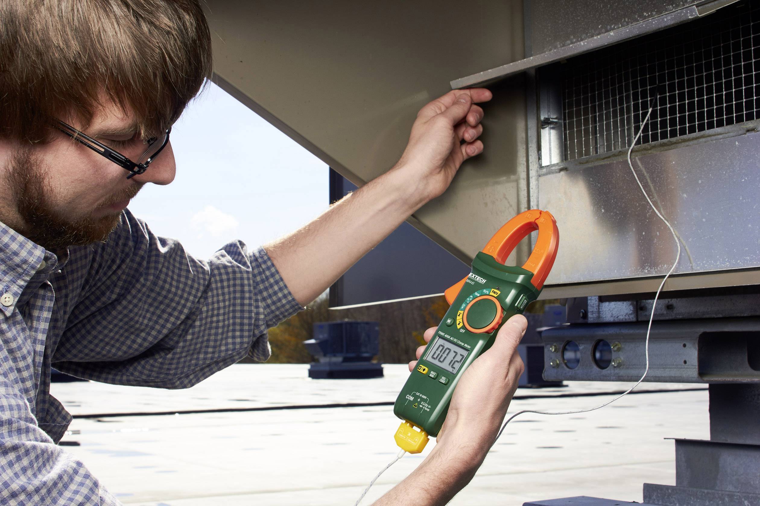 A man is checking the voltage on an industrial ventilation system using a digital measuring device.