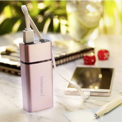A power bank is charging a smartphone on a table. In the background, a notebook, pen, and dice can be seen.