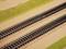Two parallel railway lines run through a sandy landscape with grass-covered hills.