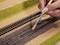 A hand is sprinkling gravel with a brush onto a model railway track to create a realistic appearance for a model railway landscape.