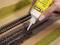 A hand is using glue from a bottle to fix model railway tracks on a landscape base plate.