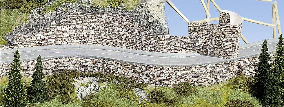 Winding road with a stone wall along a grassy slope, interspersed with trees. Scaffolding is visible in the background.