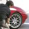 A man is checking the tyre pressure of a red car in a car park.