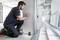 A man is kneeling and marking a line on a wall using a laser measuring device in a room under construction.