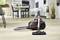 A hoover stands centrally in a modern, bright living room with wooden flooring and white furnishings.