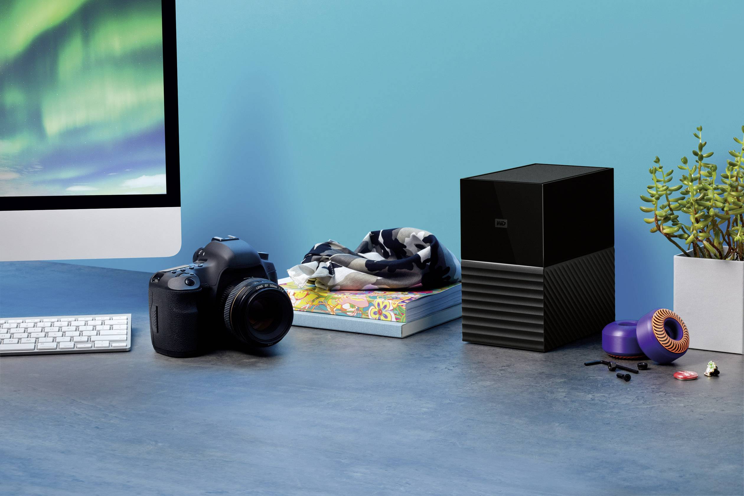 A desk with a camera, external hard drive, plants, and computer; shows a creative workspace.