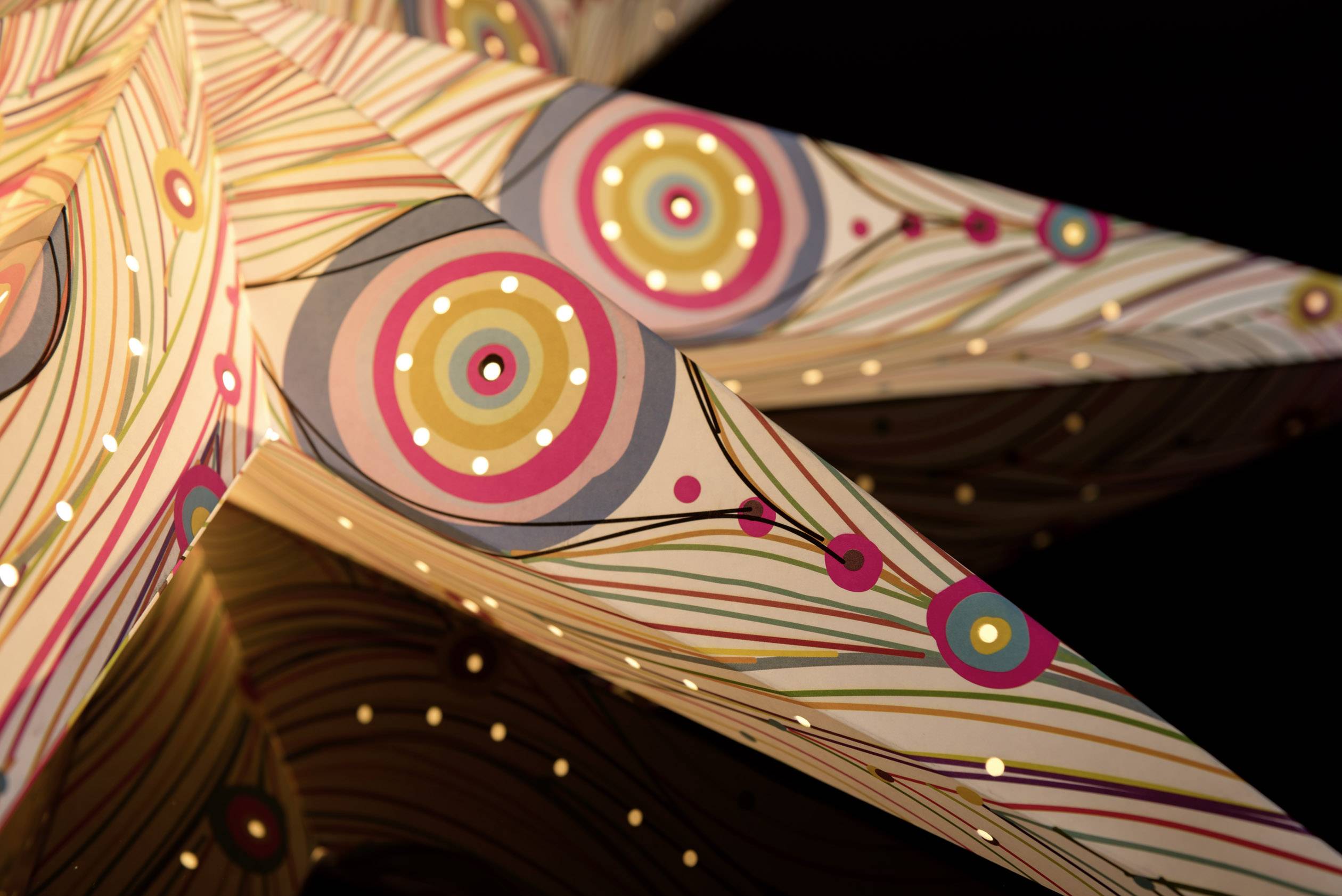 A decorative paper star with a colourful, circular pattern and small holes through which warm light shines.