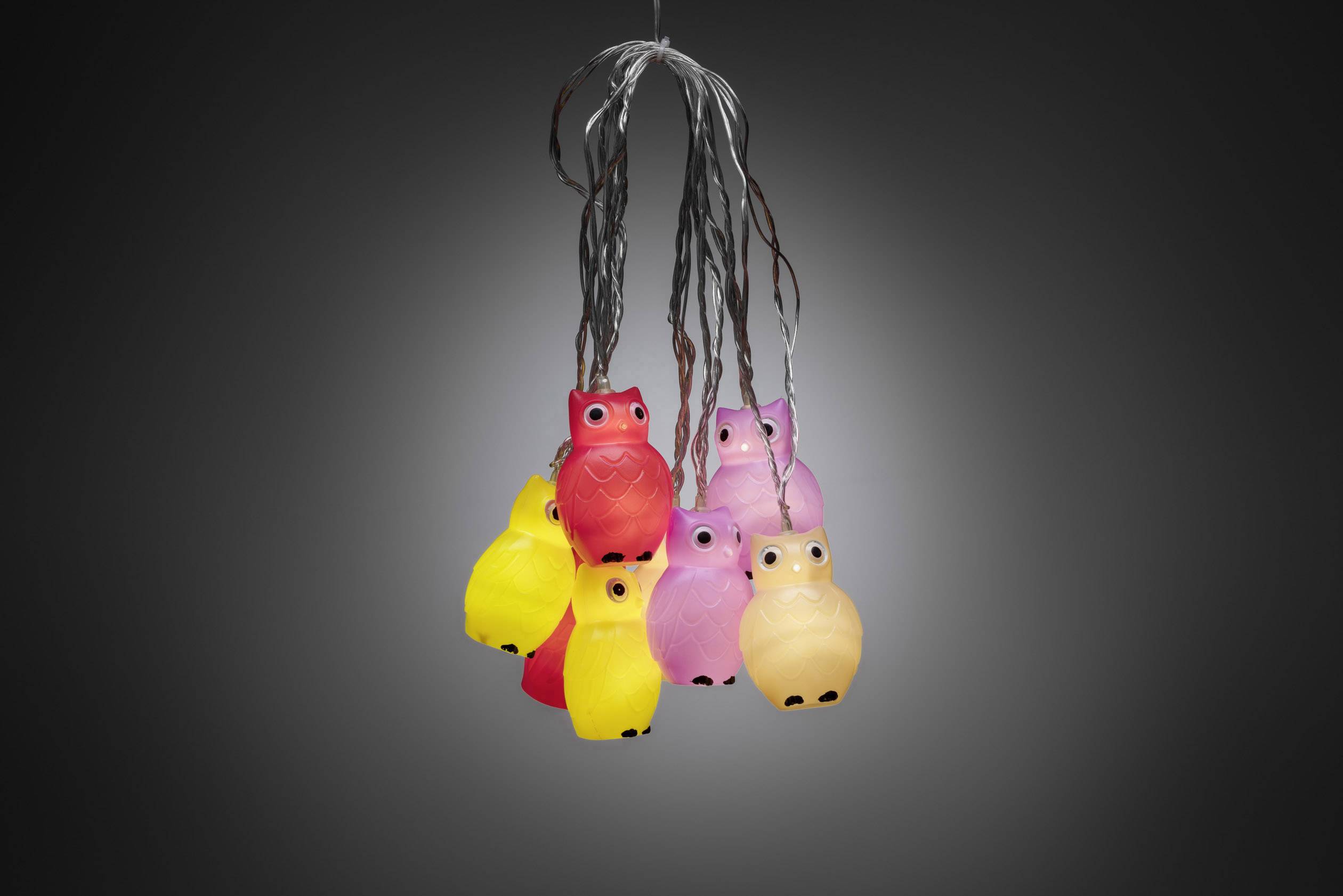Small, colourful owl-shaped lights hang together on cables against a dark background. They glow in red, pink, and yellow.