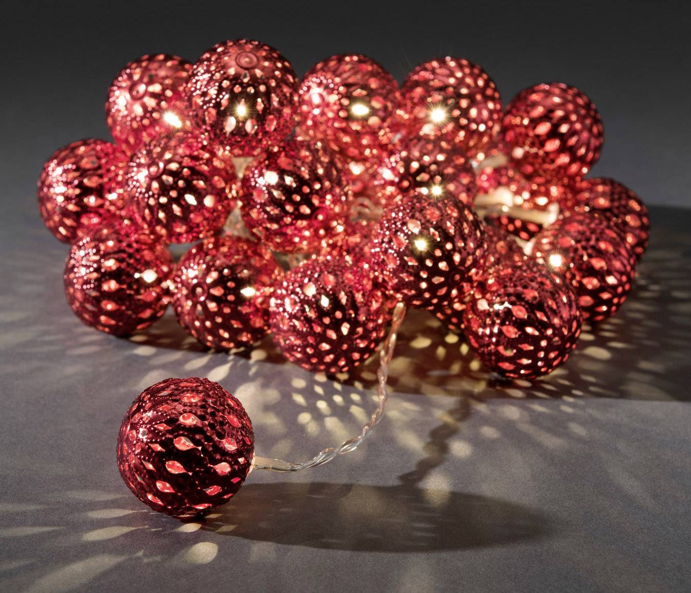 A string of fairy lights with red, spherical LED bulbs that illuminate and cast a dotted light pattern onto a dark surface.