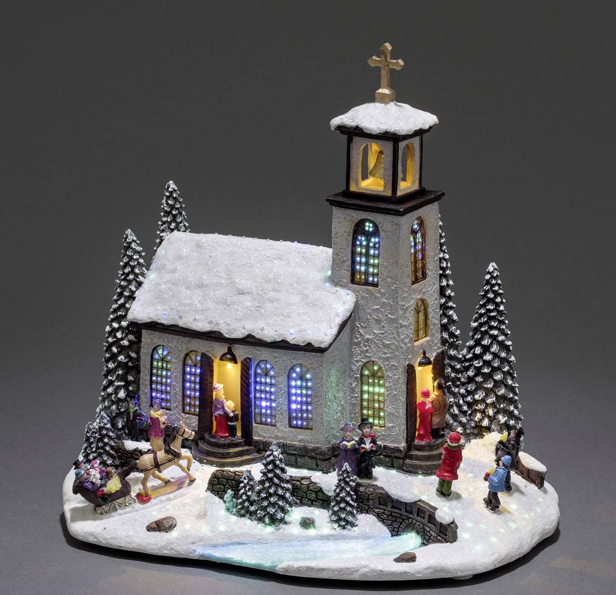A snow-covered miniature church with colourful windows and illuminated scenes of people heading to Christmas mass.