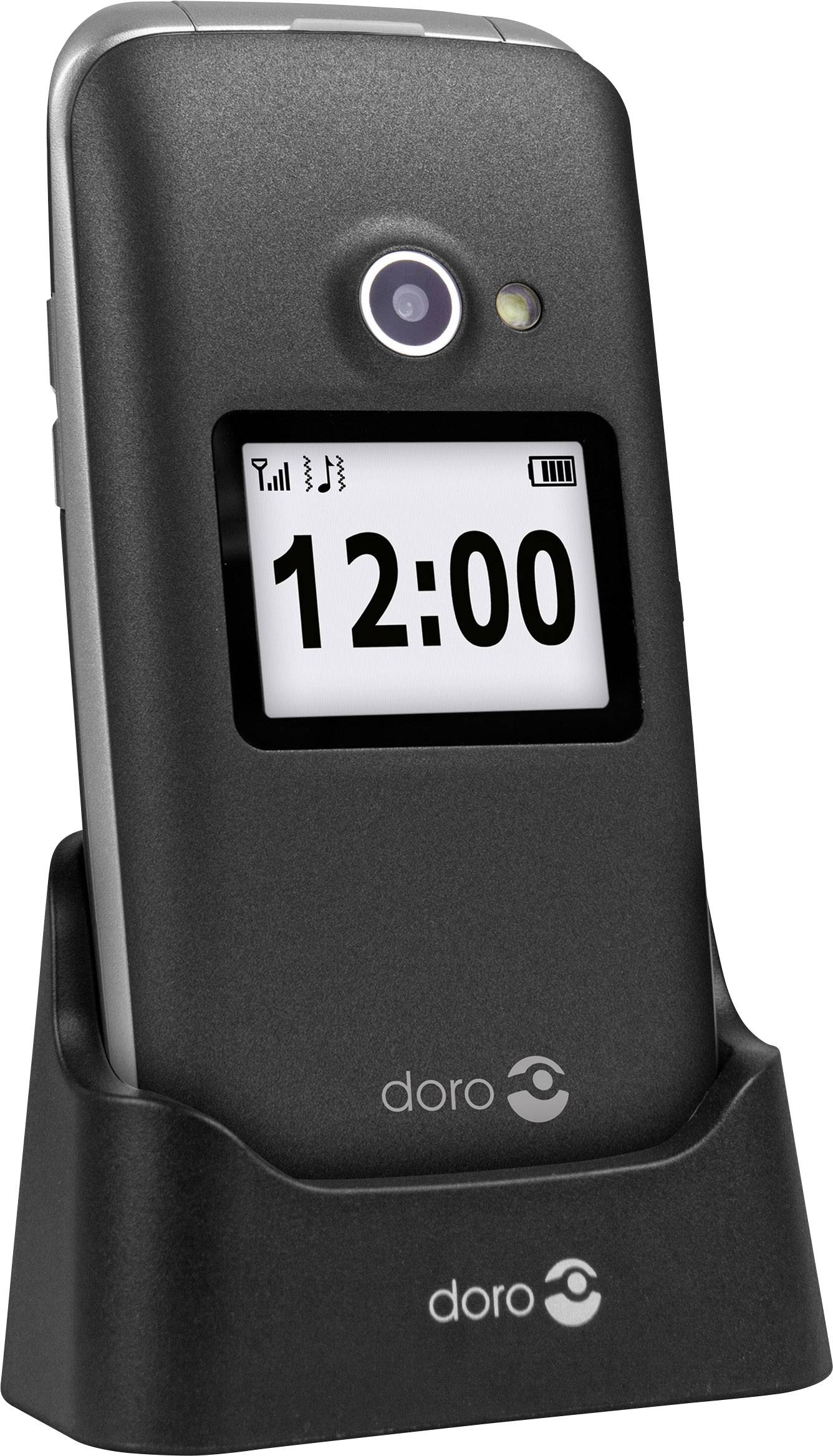 A black flip mobile phone in its charging dock displays the time 12:00 on its screen.
