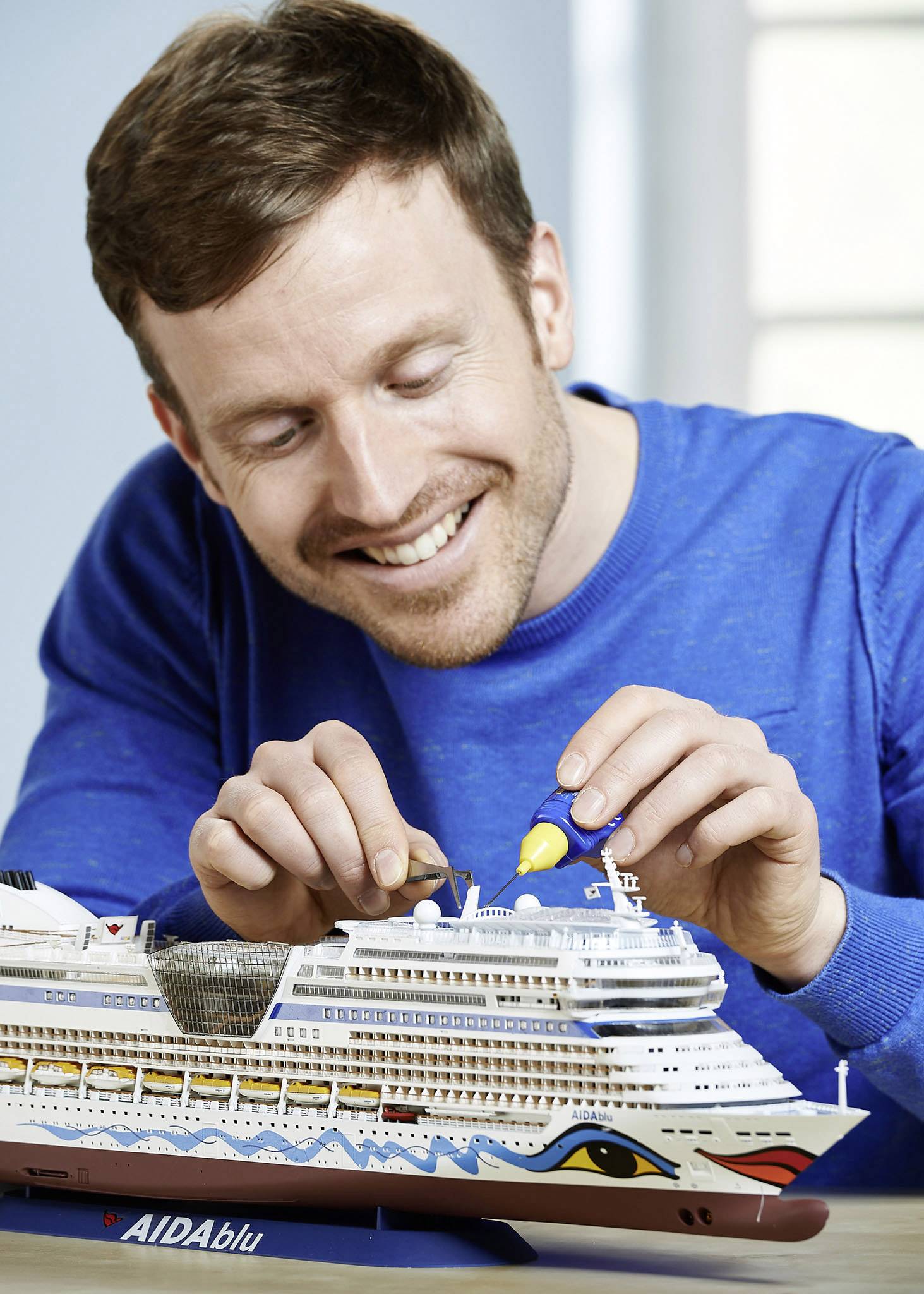 A man smiles as he carefully assembles a model ship named 'AIDAblu'.