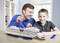 A man and a boy are building a ship model together. Both are smiling and are sitting at a table with a model of the cruise ship 'AIDABlu'.
