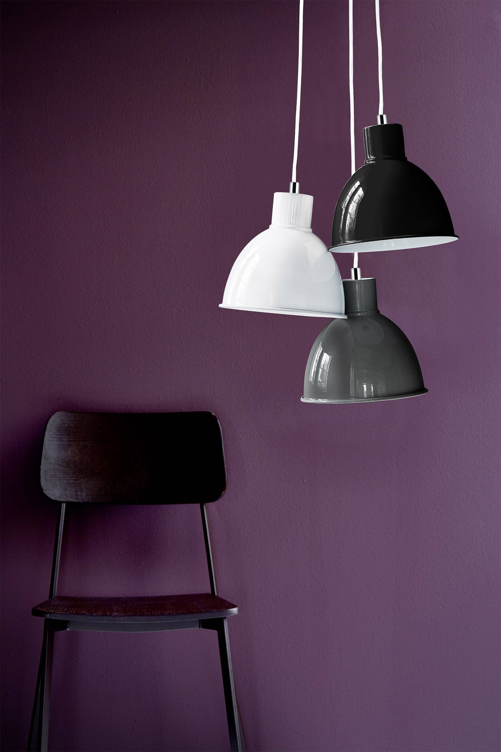 Three pendant lights in white, black, and grey hanging in front of a dark violet wall above a dark chair.