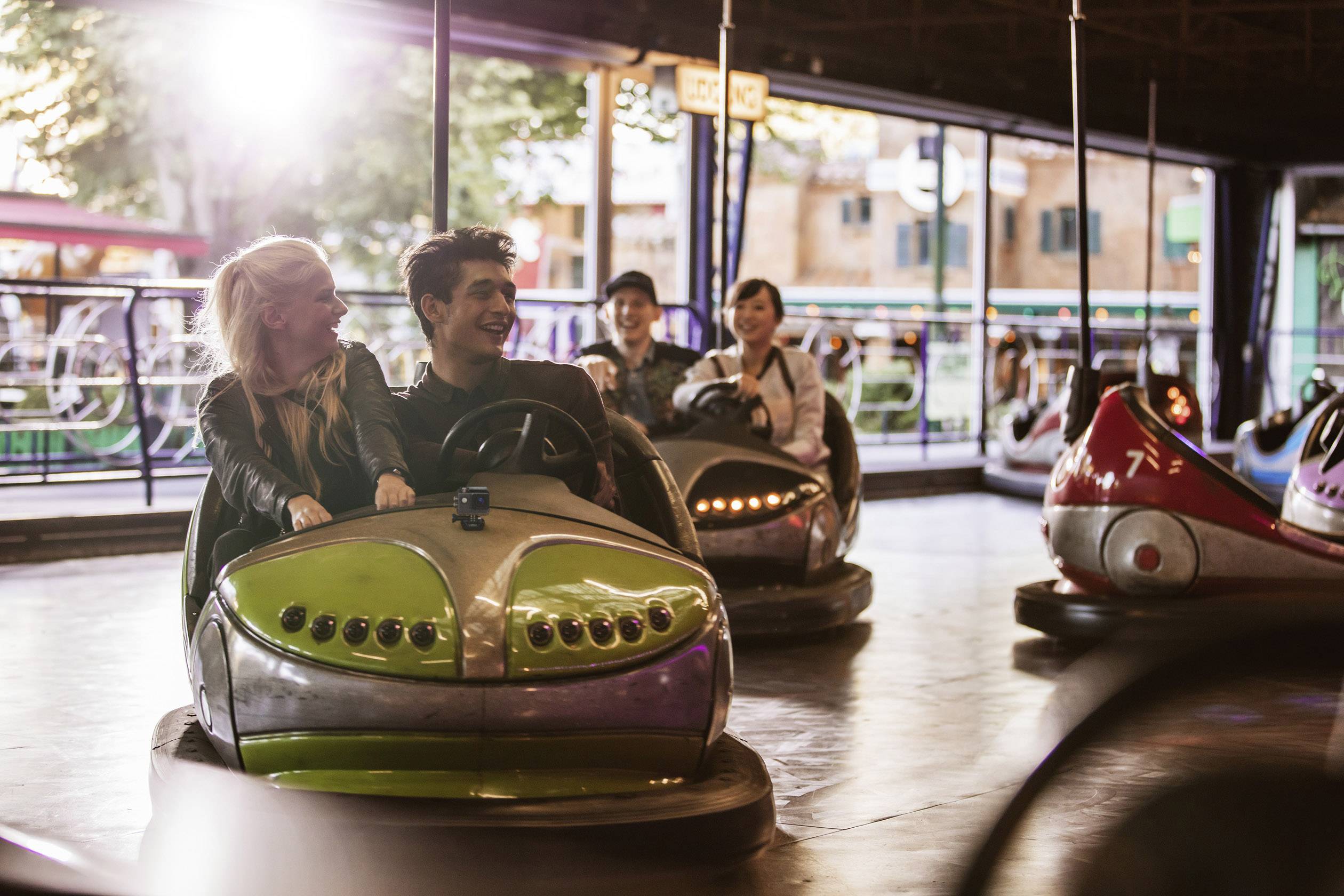 A group of young people are driving in a brightly lit dodgem arena, laughing and having fun.