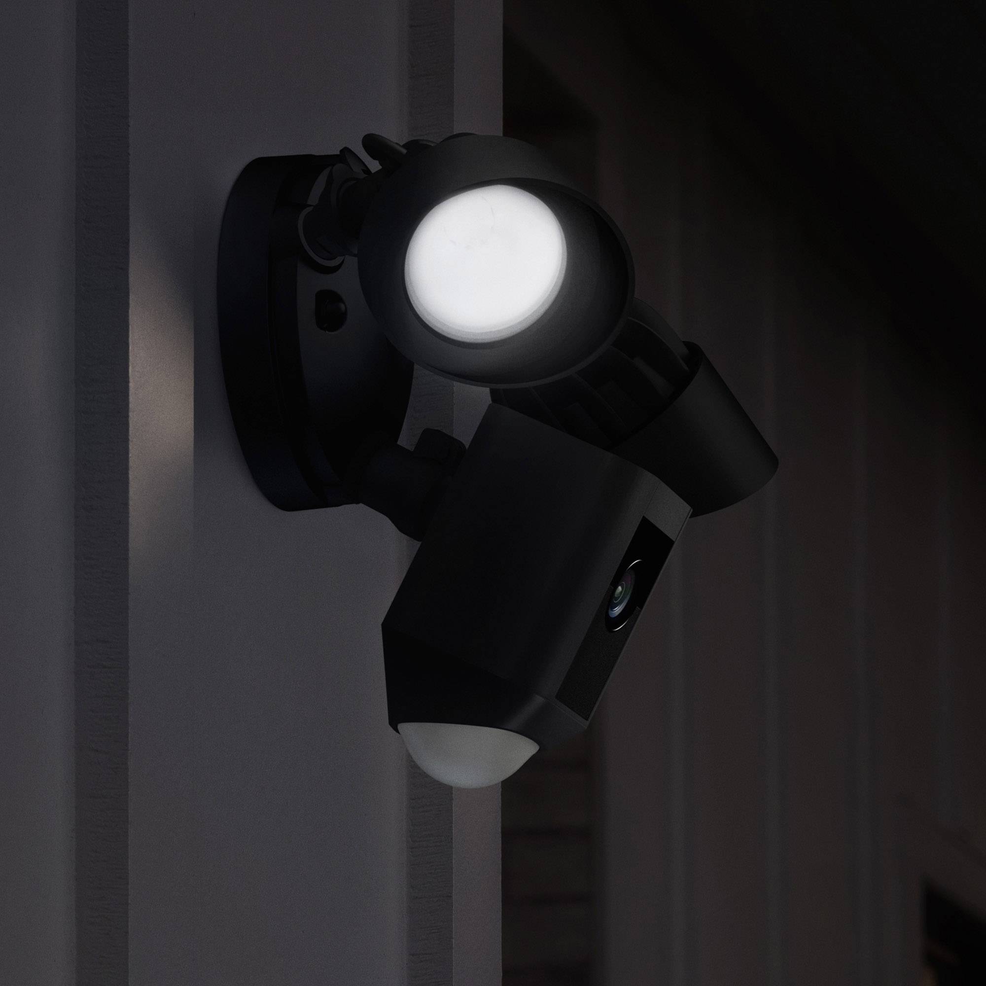 Outside light with motion sensor mounted on a house wall, illuminating in the darkness.