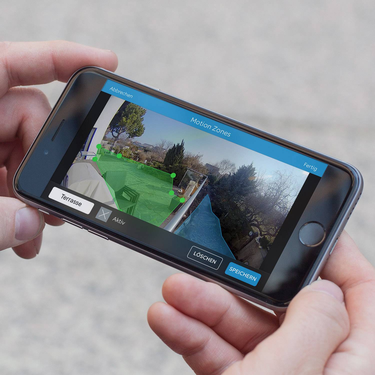A person is holding a smartphone displaying a security camera app with an activated motion zone in an outdoor area.