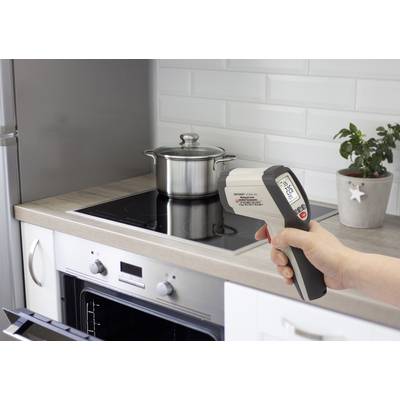 A person is holding an infrared thermometer in the kitchen, pointing it at a pot on the hob. The display shows 21.8°C.