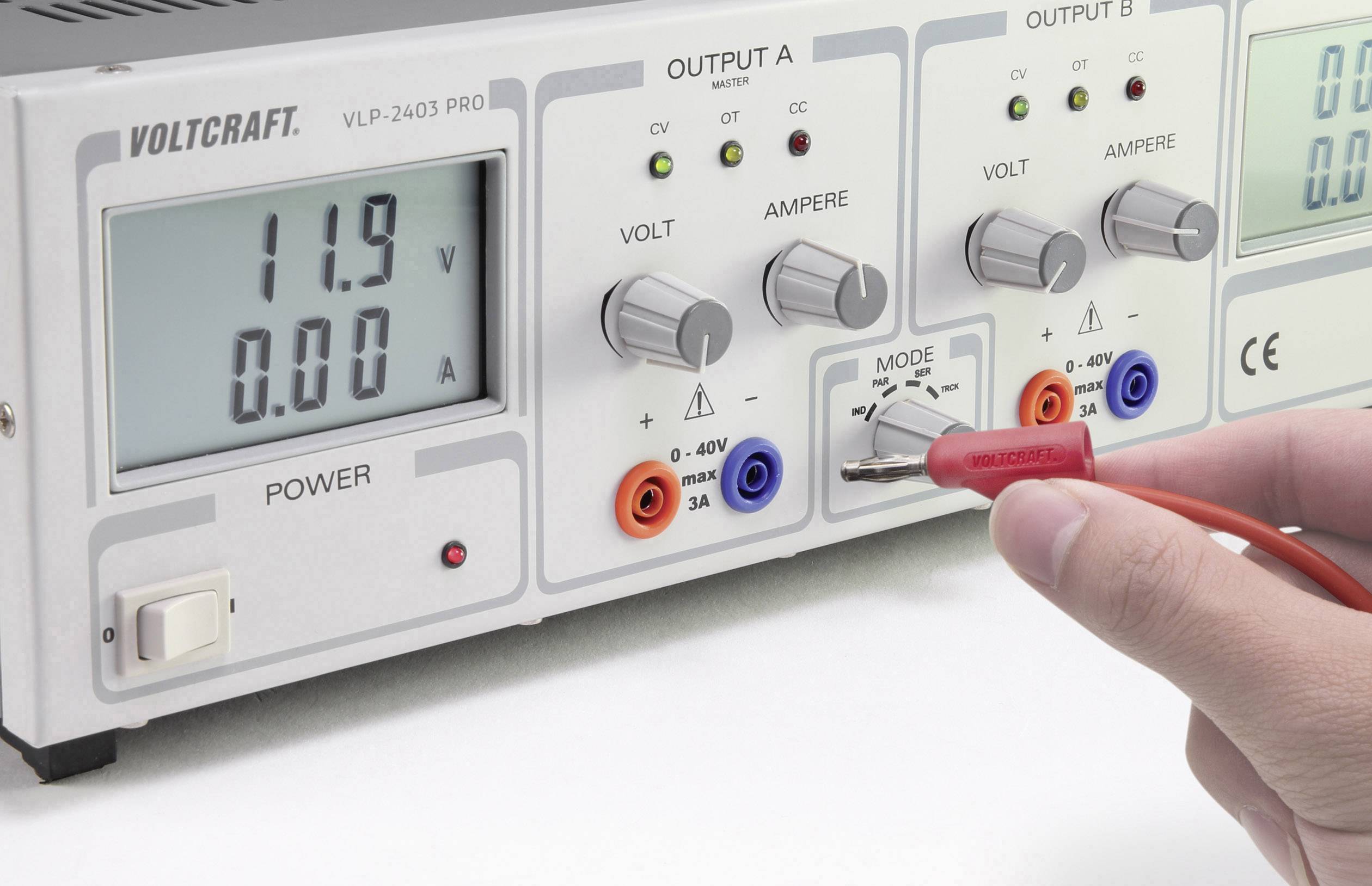 'Measuring device with digital display shows 11.9 V and 0.00 A. Control buttons for voltage, current and mode. Hand holding test probe at output.'