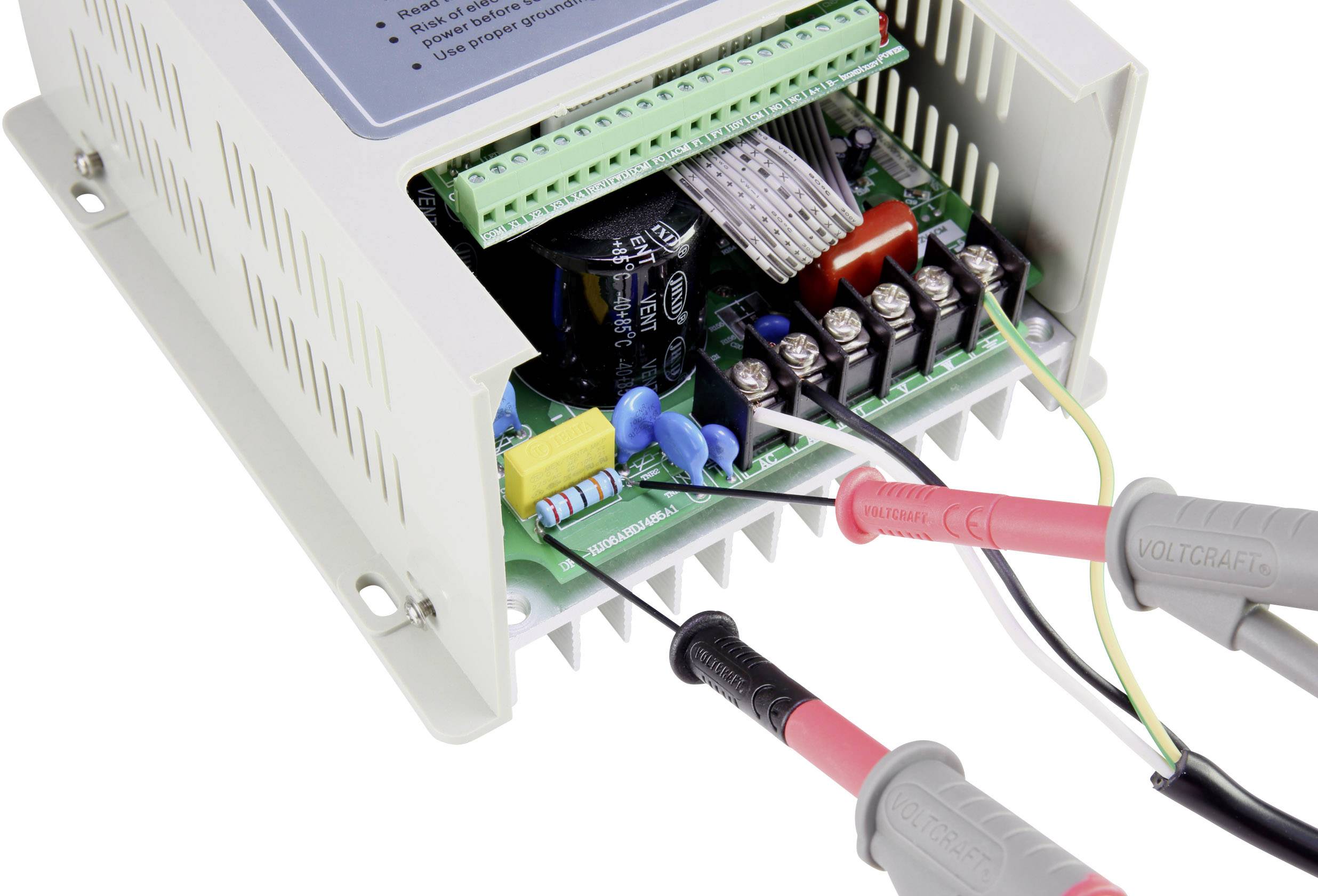 An open electronic device displays multiple cable connections and components on the circuit board. Two measurement leads are connected.