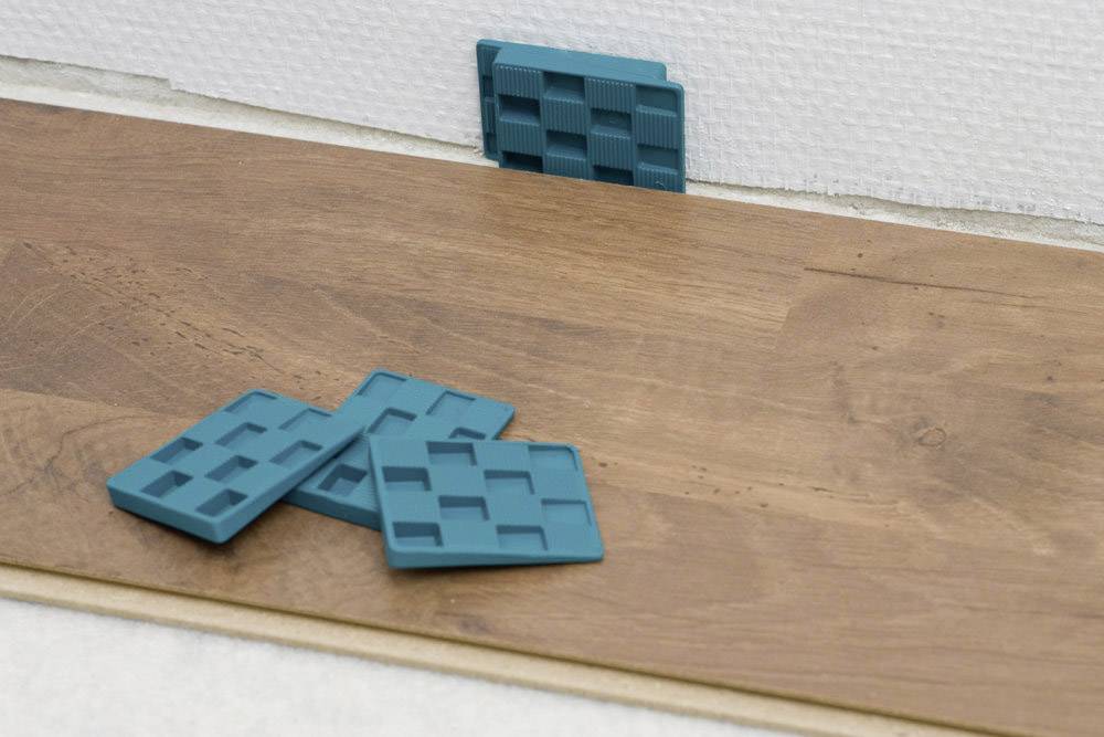 Wooden floor installation with spacers between wall and floor. Blue plastic spacers ensure an expansion gap.