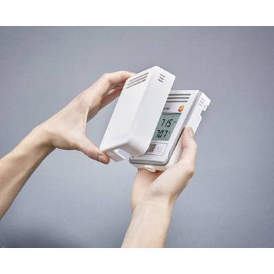 A person is holding a thermostat in their hands. The display shows a temperature of '21.5°C'. The device is in a white casing.
