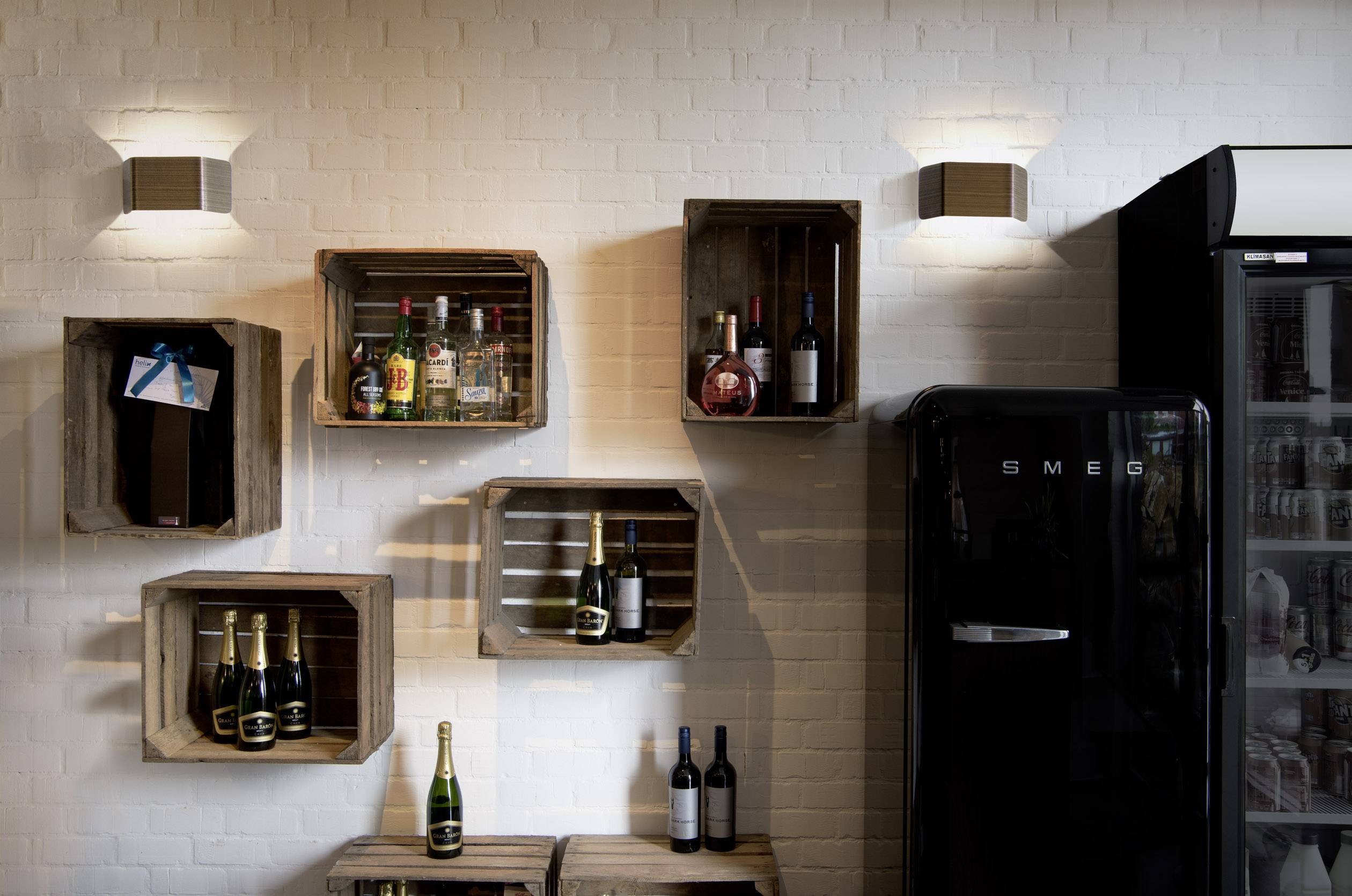 A stylish wall design with wooden shelves displaying bottles of wine and spirits, alongside a refrigerator in a retro design.
