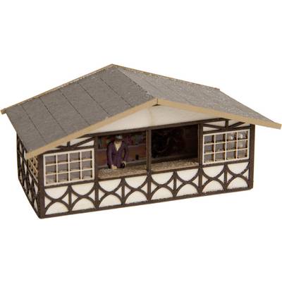 A miniature building with traditional patterns; a small person in a purple jacket stands in front with an outstretched arm.