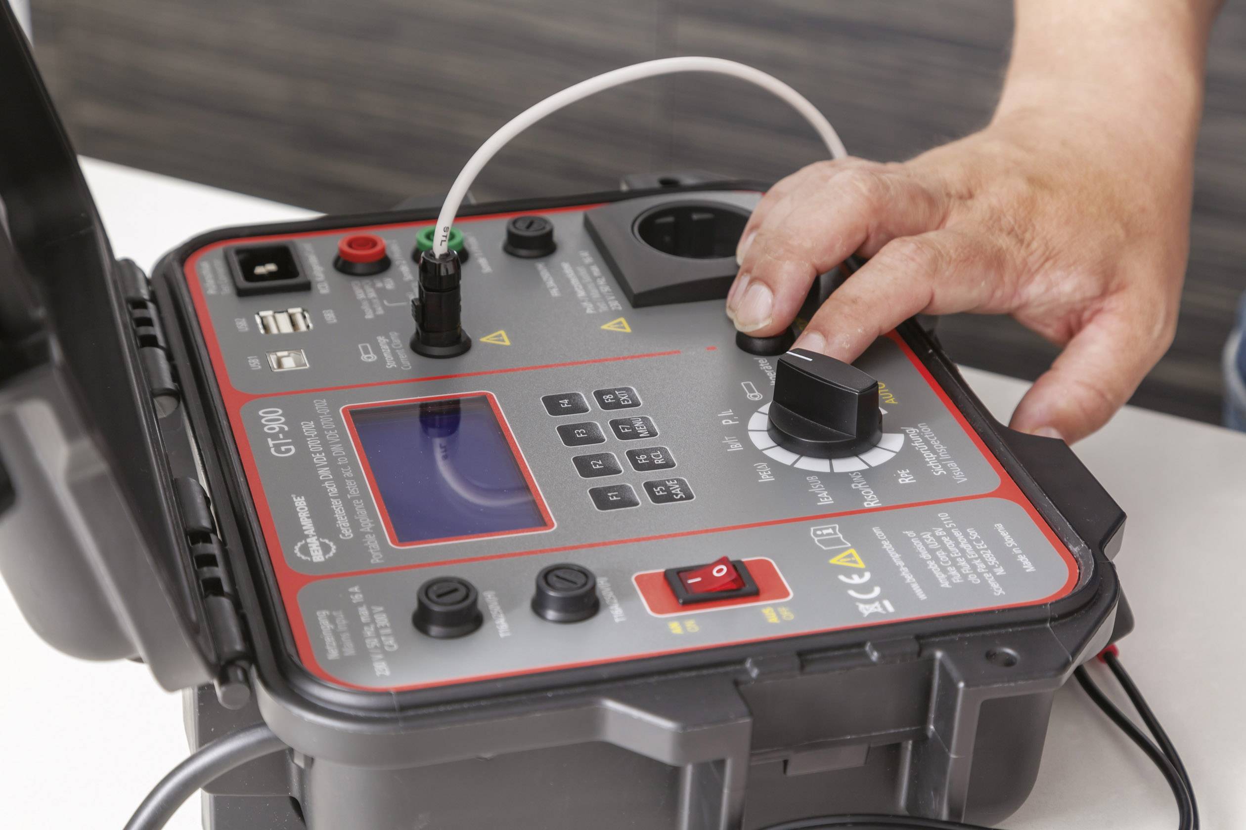 A person is operating a portable electrical testing device with buttons and displays for measuring voltage or resistance.
