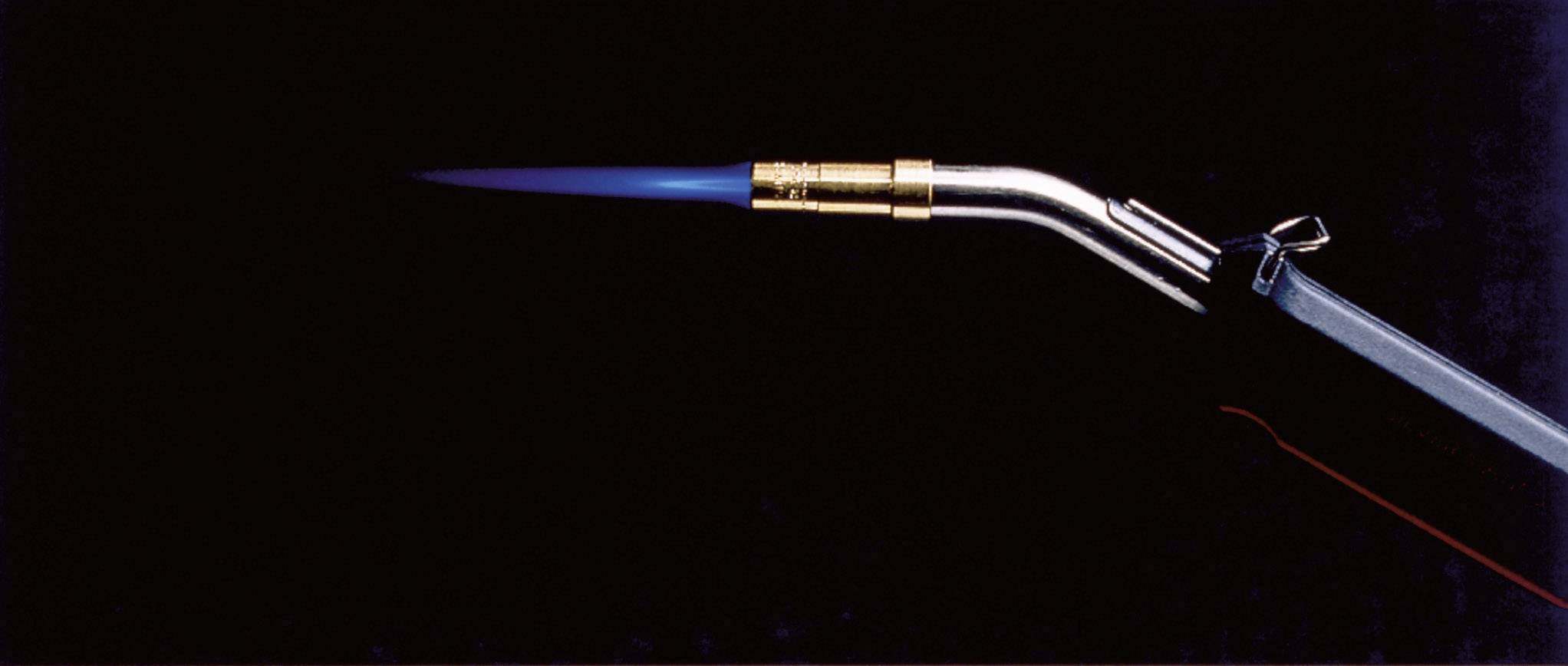 A silver burner with a blue flame on a black background, demonstrating the operation of a gas burner.