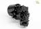 A black mechanical component with multiple edges and screws, photographed at an angle, against a white background. A logo is positioned in the top right corner.
