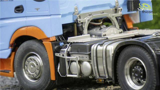 A model lorry with a blue driver's cab and orange accents. Details such as wheels and fuel tank are visible. Grass can be seen in the background.